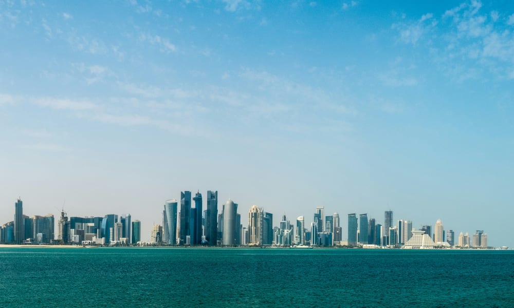 A wide view of Doha's skyline across a body of water on a clear day.