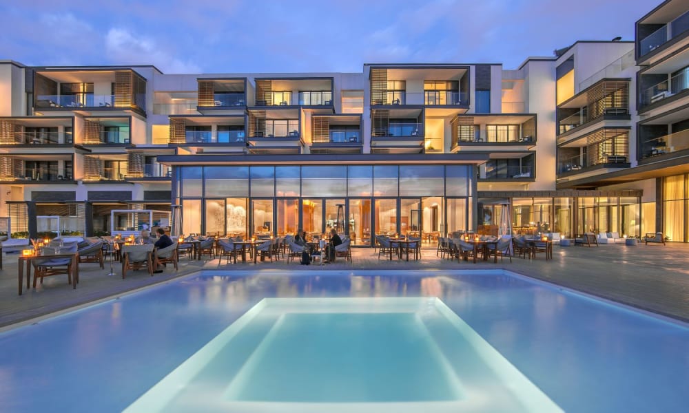 Luxuriöses Nikki Beach Resort und Spa Dubai bei Dämmerung beleuchtet, mit einladendem Swimmingpool im Vordergrund.