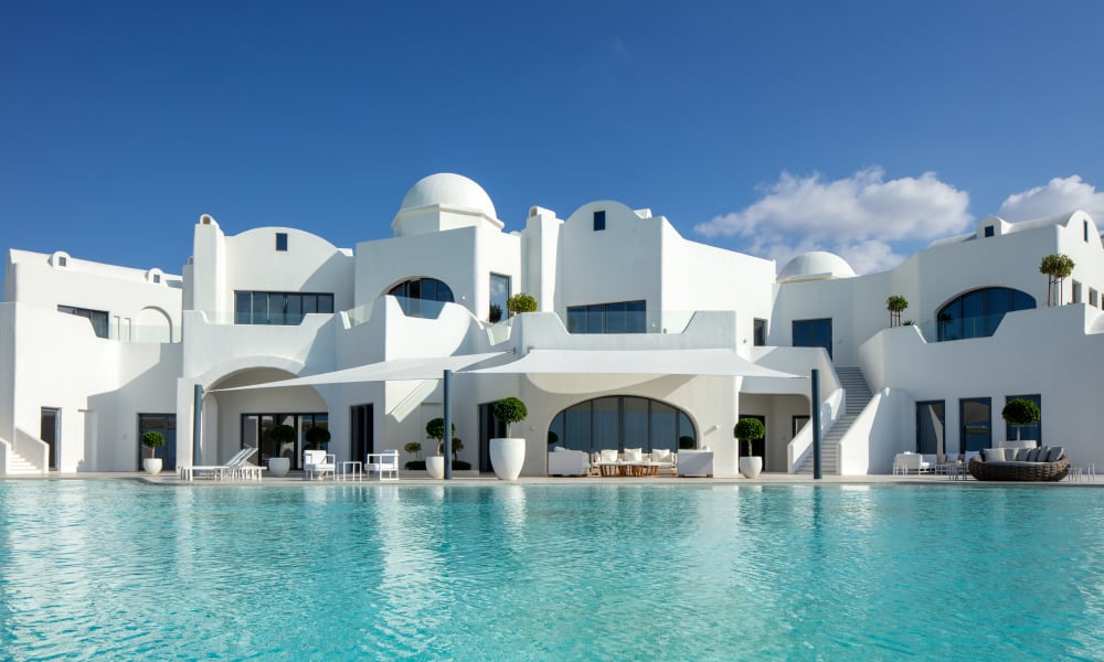Ein luxuriöses weißes Hotel mit runder Architektur und großen Glasfenstern am Pool unter einem blauen Himmel.