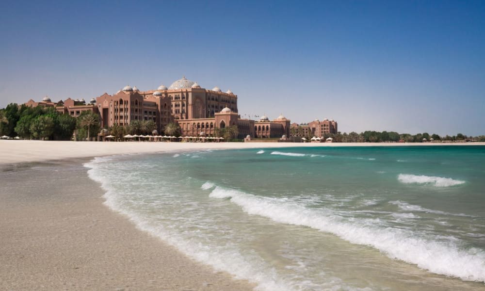 Luxurious hotel and resort buildings near a sandy beach with turquoise waters under a clear blue sky.
