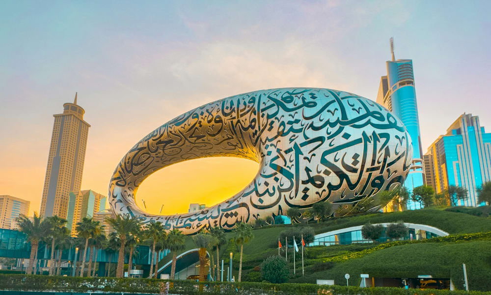 Das Museum der Zukunft in Dubai, ein futuristisches Gebäude in Form einer elliptischen Schleife mit arabischer Kalligraphie an der Fassade, vor einer Stadt skyline bei Sonnenuntergang.