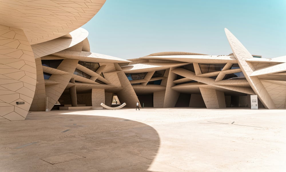 Modernes architektonisches Design des Doha National Museum mit komplexen, organischen Formen und offenem Raum unter klarem Himmel.