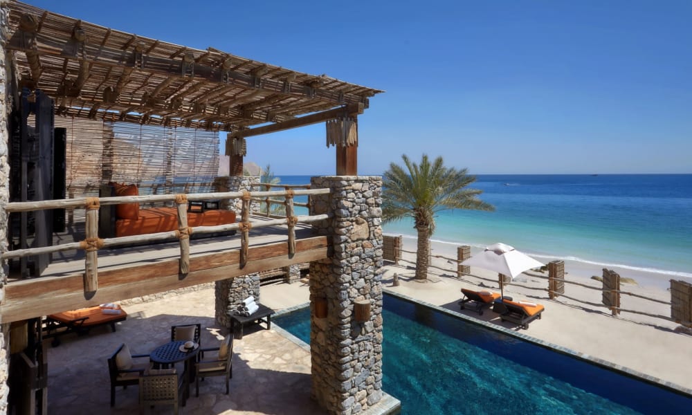 Ein luxuriöses Strandresort mit einem Pool, Sitzbereich und einem Balkon mit Blick auf den Sandstrand und den Ozean.