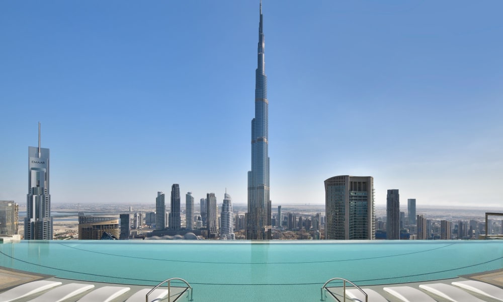 A rooftop swimming pool offers a view of the Burj Khalifa and Dubai skyline under a clear blue sky.