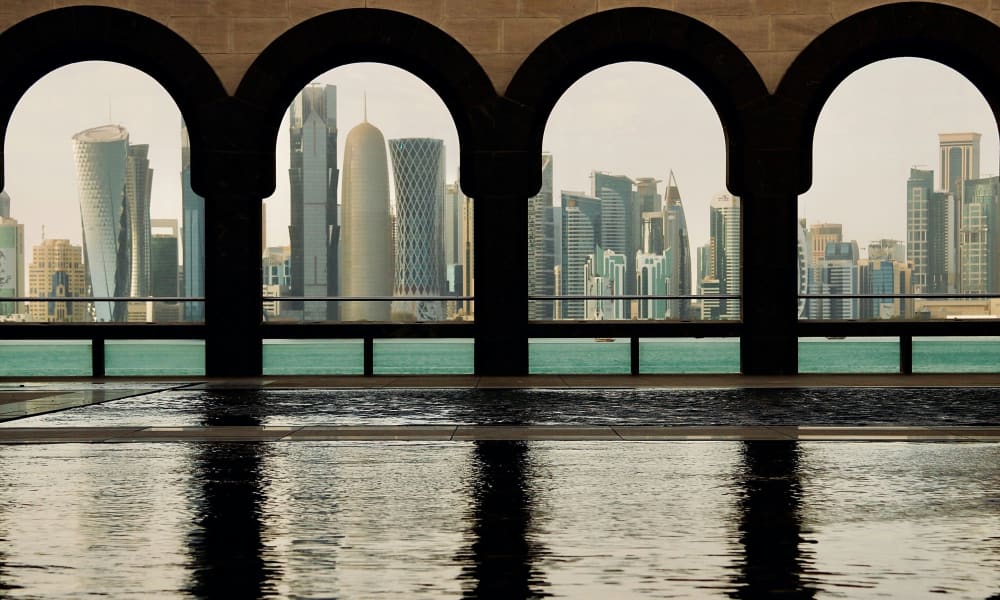View of Doha's skyline through arched windows with a pool in the foreground.