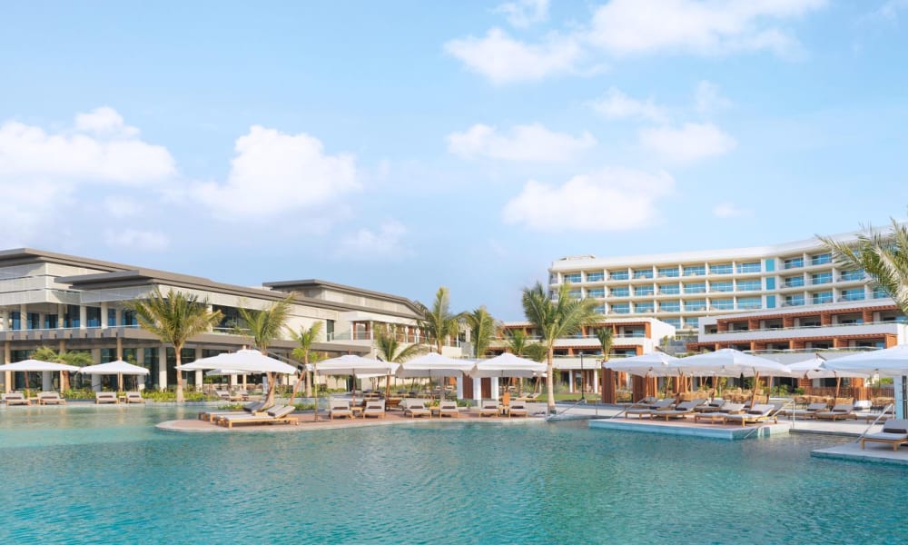 Luxury resort with swimming pool, palm trees, and sun umbrellas in a coastal setting.
