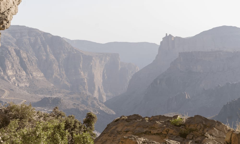 A view of deep canyon with steep rocky cliffs and sparse vegetation in a desert landscape.