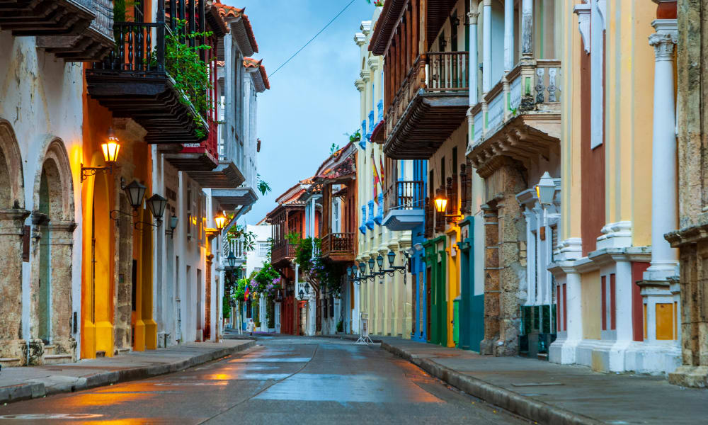 Leere historische Straße in Cartagena bei Dämmerung mit bunten kolonialen Gebäuden und beleuchteten Straßenlaternen, die sich auf dem nassen Pflaster spiegeln.