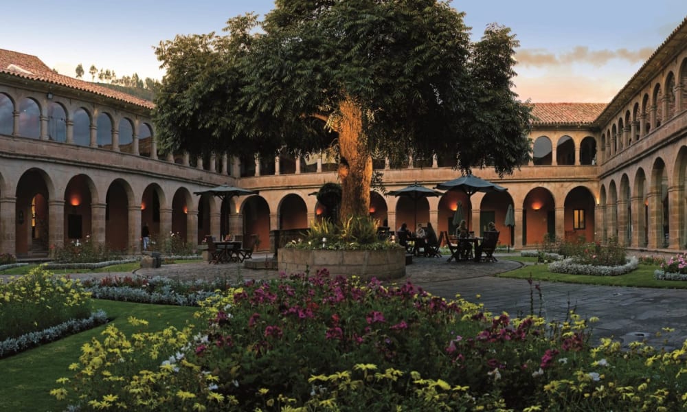 Ein historischer Kreuzgang mit zentralem Garten und umlaufenden Bögen bei Sonnenuntergang.