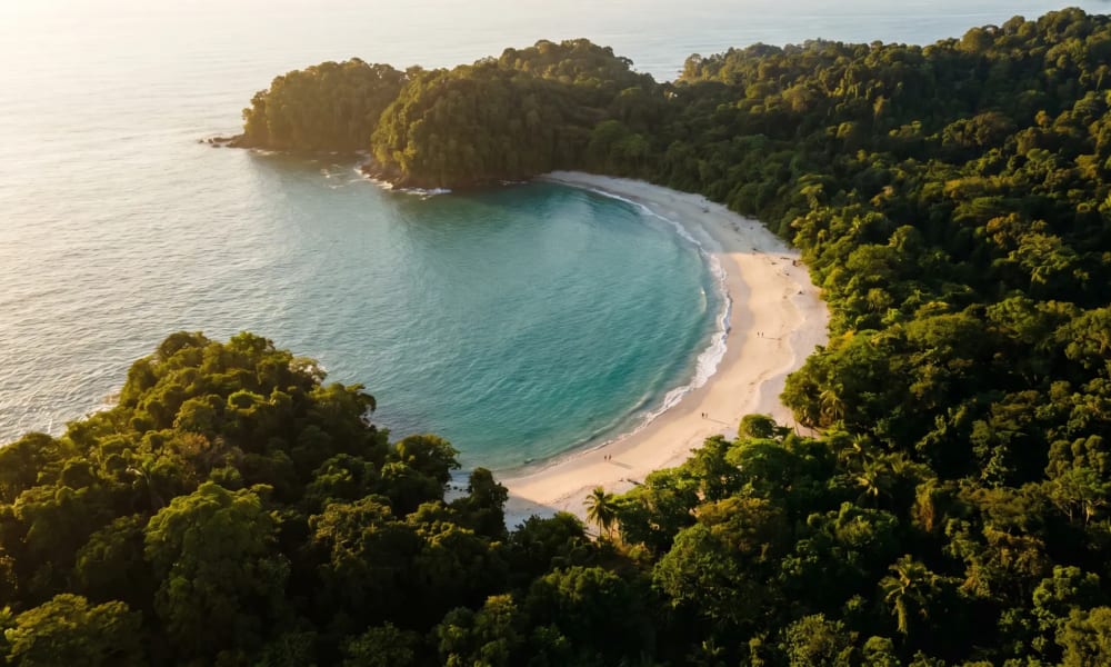 Hufeisenförmige Bucht von Playa Manuel Antonio mit türkisem Wasser und Regenwald im Morgenlicht