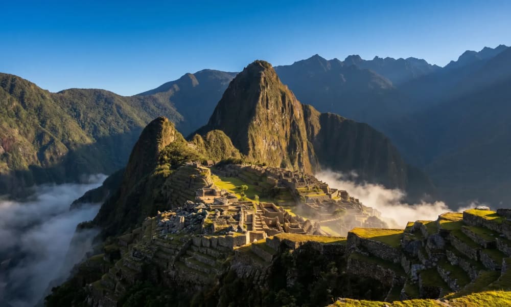 Antike Inka-Ruinen von Machu Picchu im Sonnenlicht beleuchtet, umgeben von Bergen und Wolken unter der Stätte.