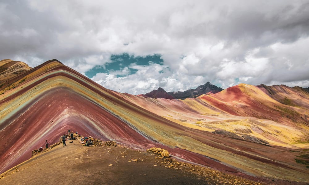 Bunte Regenbogenberge in Peru mit lebhaften Streifen in Rot, Gelb und Grün unter bewölktem Himmel.