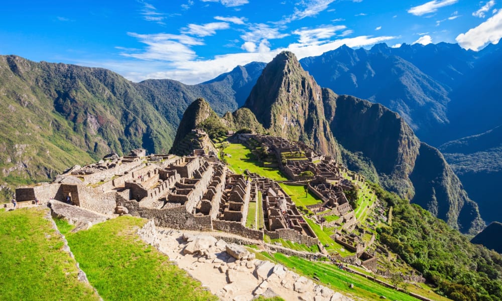 Ancient Incan ruins of Machu Picchu with lush green terraces and mountainous backdrop under a bright blue sky.