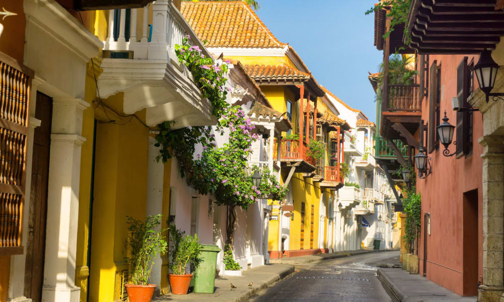 Bunte koloniale Gebäude säumen eine enge Straße in der Altstadt von Cartagena, mit Topfpflanzen und Holzterrassen.