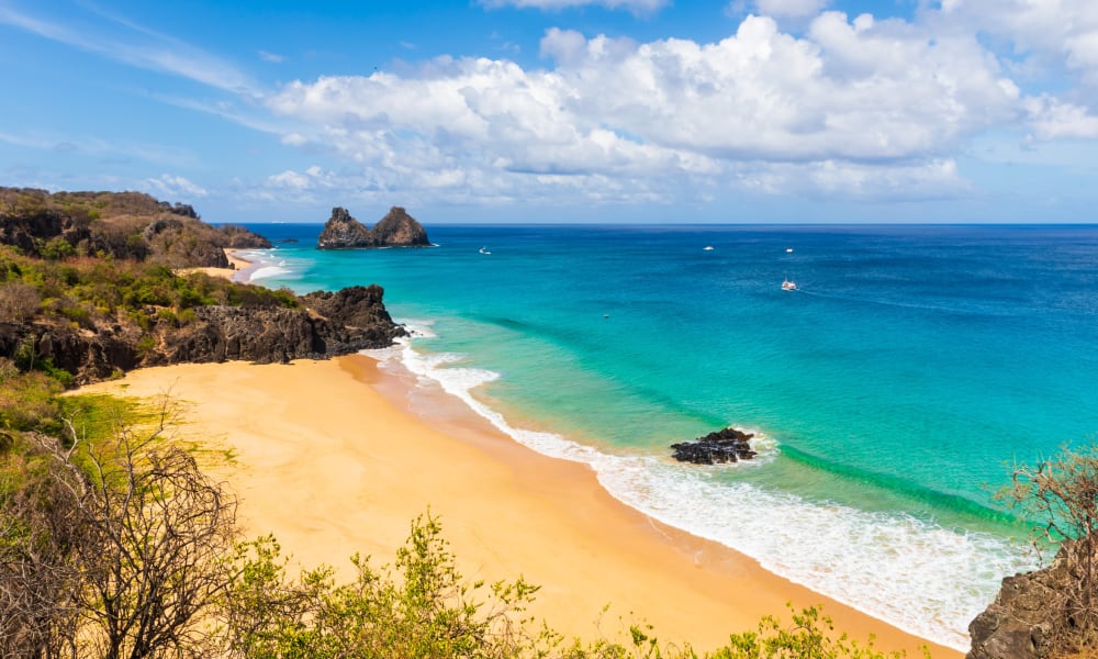 Beautiful sandy beach with turquoise waters and rocky formations, viewed from a high vantage point on a sunny day.