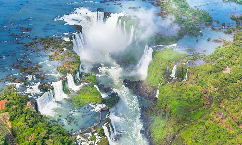 Aerial view of Iguazu Falls surrounded by lush green forest and flowing water channels in Brazil.