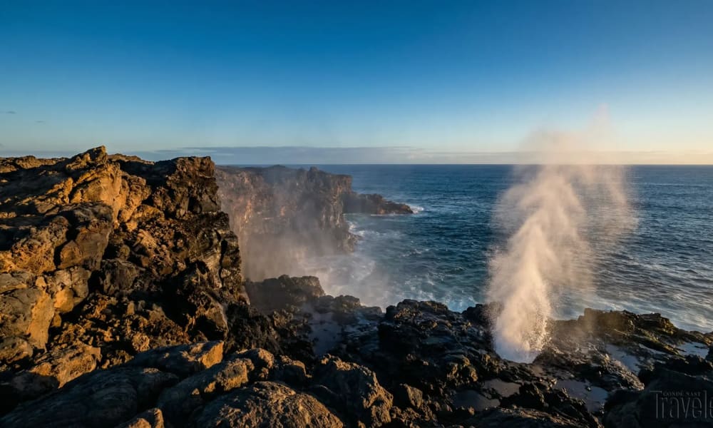 Steilklippen auf der Insel Española im Galápagos-Archipel mit Sprühfontäne des Blowholes bei Sonnenuntergang