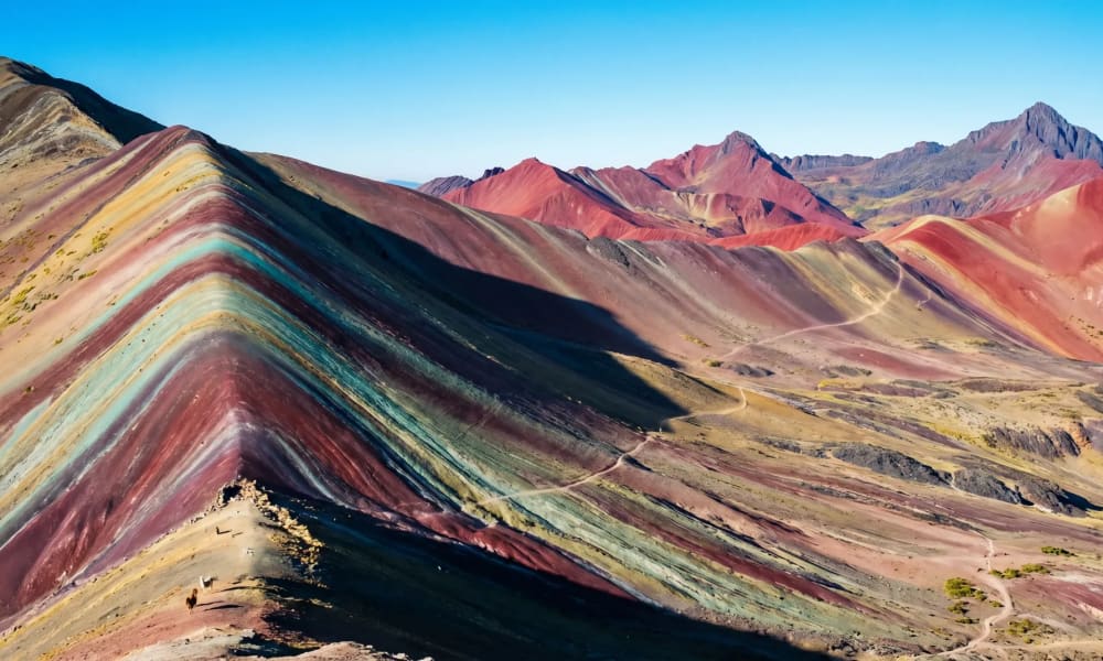 Vinicunca Rainbow Mountain in Peru mit roten, gelben und türkisen Mineralschichten im Morgenlicht vor den Anden