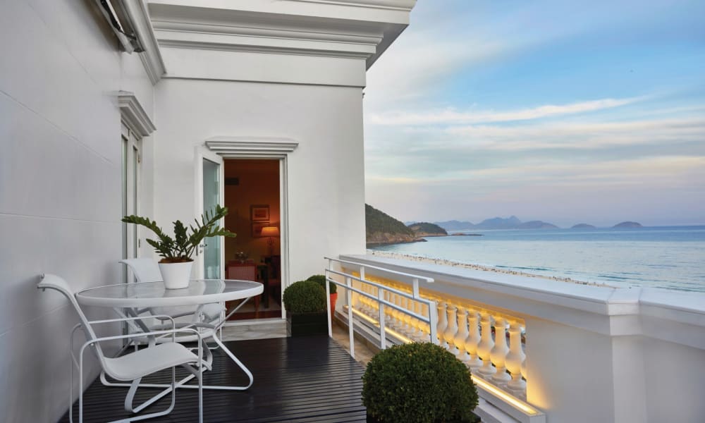 A balcony with white furniture overlooking the beach and ocean in Rio de Janeiro, Brazil.