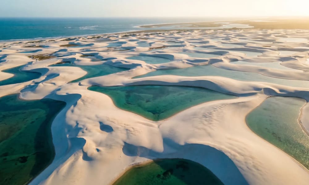 Luftaufnahme der Lençóis Maranhenses in Brasilien mit weißen Dünen und türkisen Süßwasserlagunen im goldenen Abendlicht