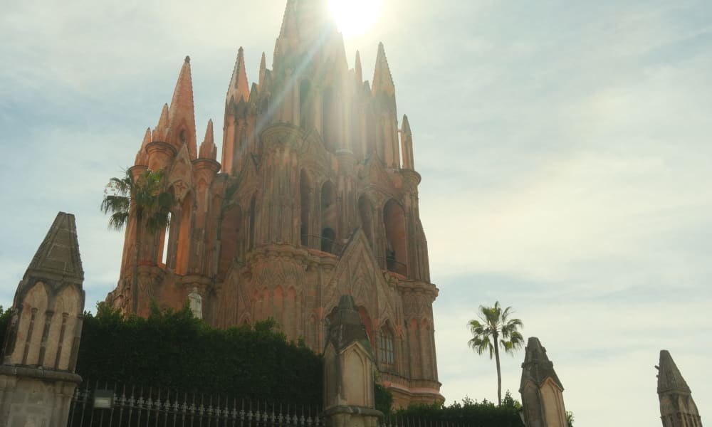 Kirche in San Miguel de Allende, Mexiko, mit hohen gotischen Türmen unter hellerer Sonne und teilweise bewölktem Himmel.