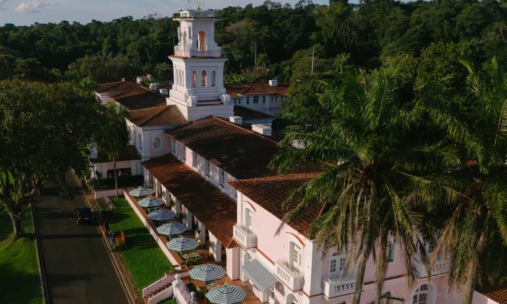 Luftaufnahme des Hotel das Cataratas, umgeben von üppigem Grün und Palmen, mit einem markanten weißen Glockenturm und mehreren Sonnenschirmen auf der Terrasse.