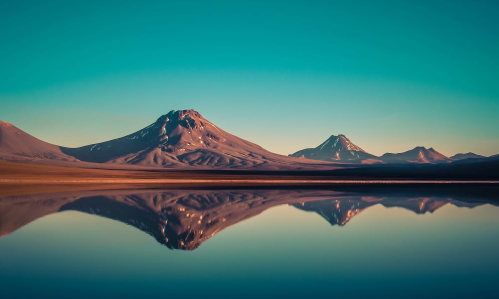 Eine ruhige Landschaft mit vulkanischen Bergen, die in einem stillen See im Morgengrauen in der Atacama-Wüste gespiegelt werden.