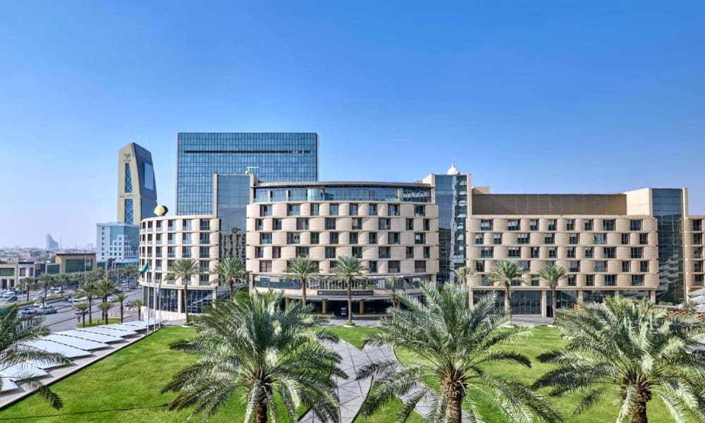 Moderne Hotelgebäude mit Palmen im Vordergrund, vor klarem blauen Himmel in Riyadh.