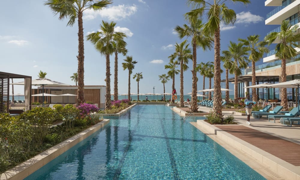 Ein luxuriöser Pool in einem modernen Hotel in Dubai mit Palmen und Strandblick.