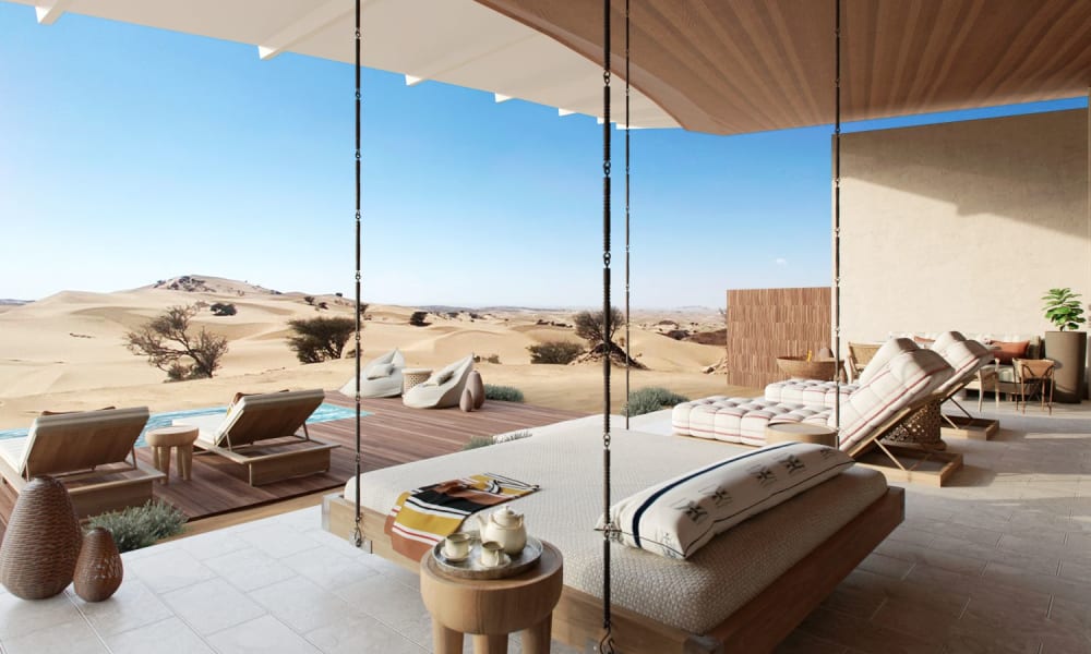 Open-air lounge with swing seats overlooking a desert landscape with sand dunes and sparse vegetation.