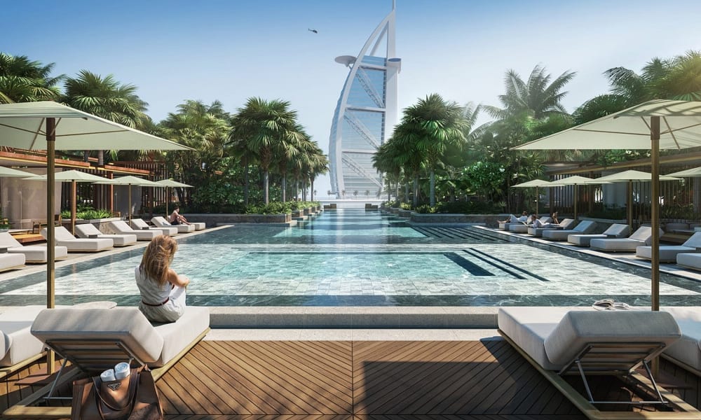 Luxurious poolside scene with lounge chairs and umbrellas at a high-end resort, with the Burj Al Arab in the background.