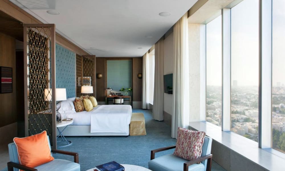 Luxury hotel suite with large windows offering a city view, modern furniture, and elegant decor.