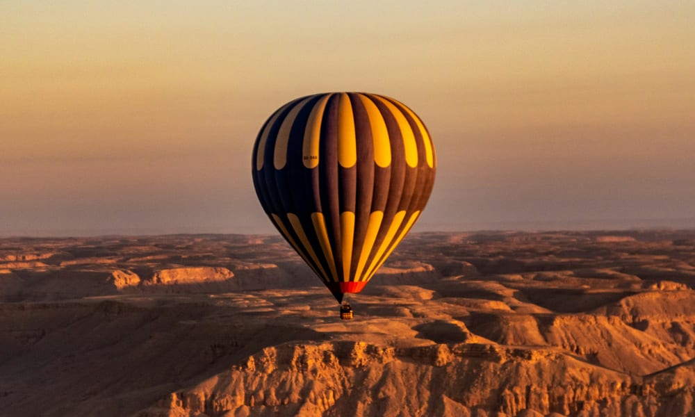 Ein Heißluftballon schwebt über einer Wüstenlandschaft bei Sonnenuntergang.