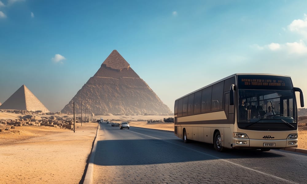A coach bus driving on a road with pyramids in the background in Egypt.