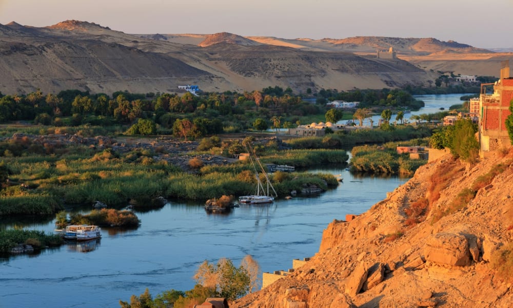 Eine landschaftliche Aussicht auf den Nil mit Booten, grünen Ufern und Wüstenhügeln in Ägypten.