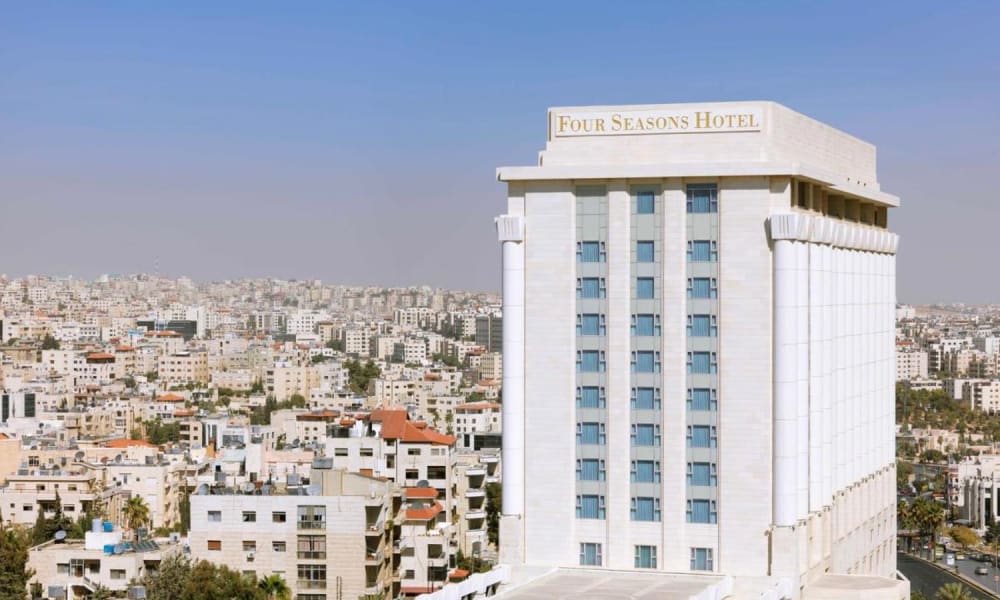 Ein hohes, weißes Four Seasons Hotel Gebäude ragt in einer Stadtlandschaft mit vielen kleineren Gebäuden im Hintergrund während des Tages auf.
