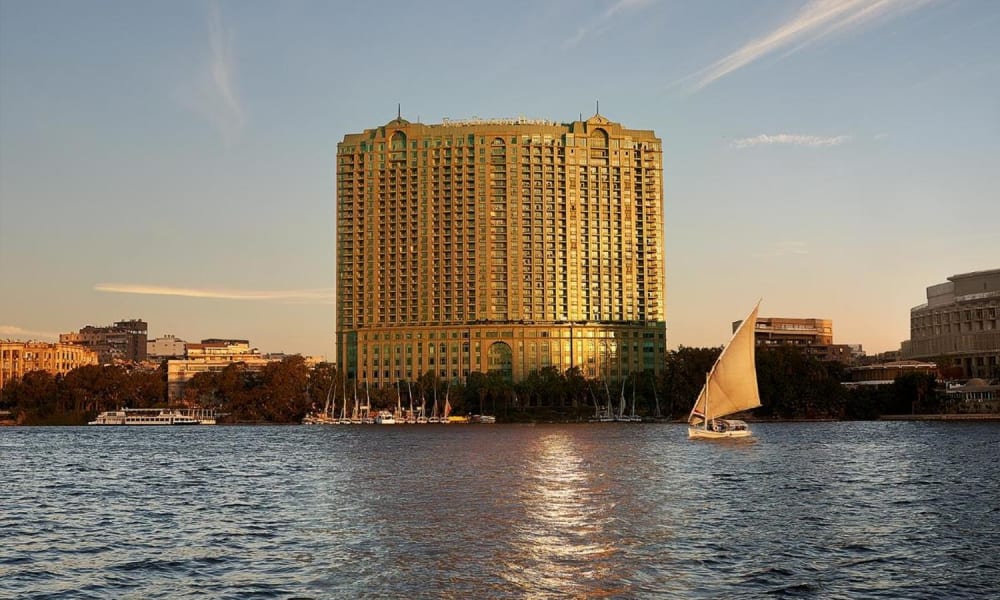 Das Four Seasons Hotel Cairo am Nile Plaza steht hoch am Nil während der goldenen Stunde, mit seiner Glasfassade, die das warme Sonnenlicht widerspiegelt.