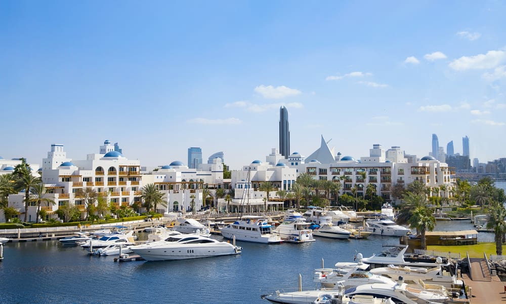 Yachthafen mit Booten vor dem Park Hyatt Dubai Hotel mit weißen Gebäuden und Palmen unter klarem blauem Himmel.