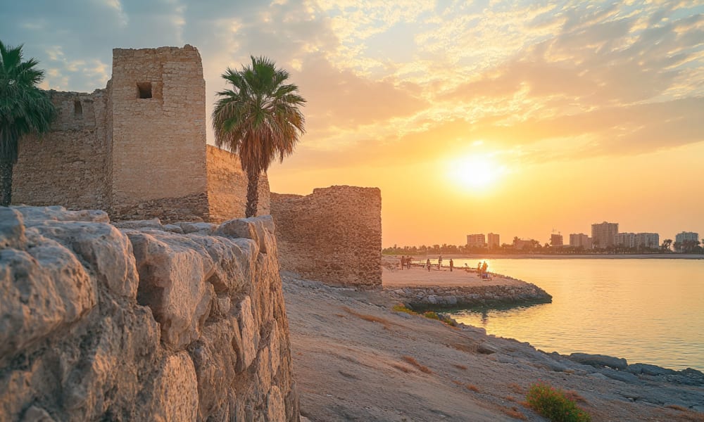 Ancient stone fortress with palm trees at sunset by the waterfront in Bahrain.