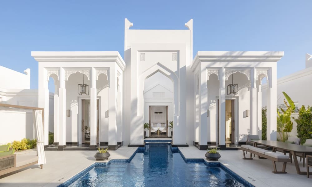 Ein eleganter weißer Palast mit islamischen Architekturelementen, mit einem zentralen Brunnen und einem reflektierenden Pool im Vorderhof.