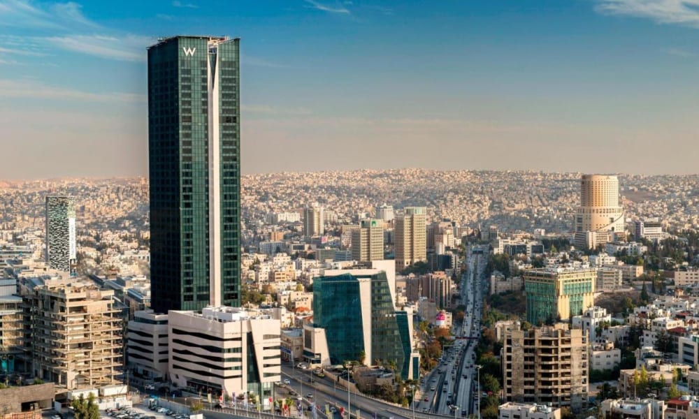 Stadtbild von Amman mit hohen modernen Gebäuden und Autobahnen unter einem blauen Himmel.