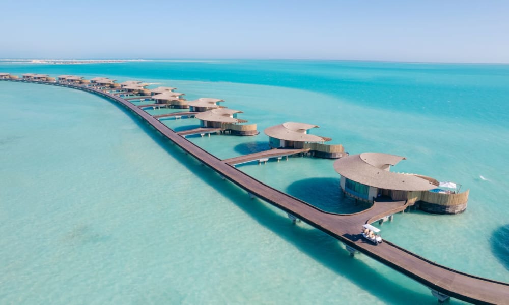 Luftaufnahme von Wasserbungalows, die durch einen Steg an einem Resort am Roten Meer verbunden sind, mit türkisfarbenem Wasser.
