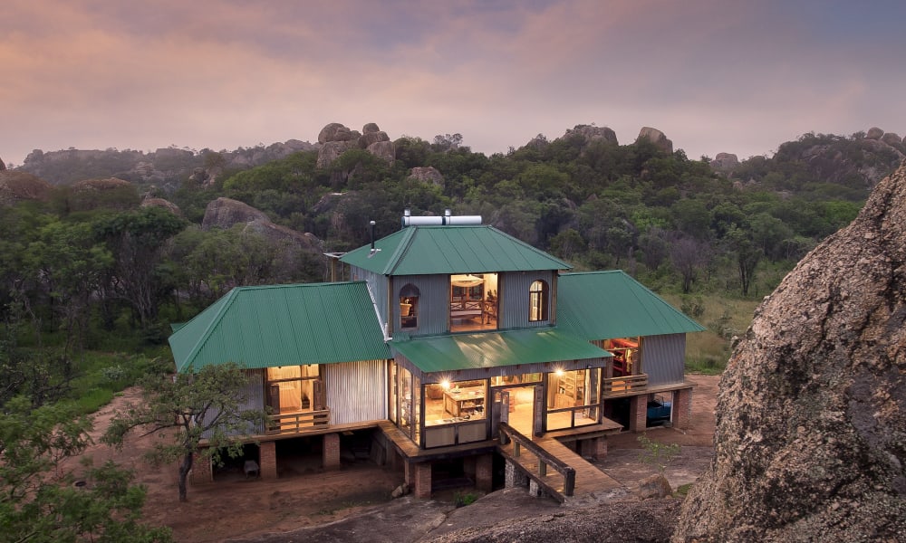 Ein gemütliches Haus mit grünem Dach, das zwischen Felsen und dichten Bäumen in den Matobo-Hügeln liegt.