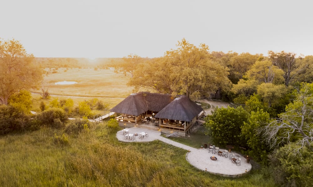 Aerial view of a main lodge surrounded by trees and grasslands at sunset in a wildlife reserve.