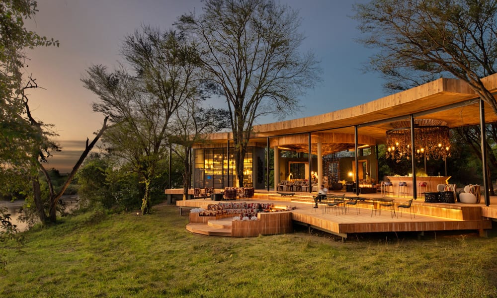 Luxus-Gästebereich mit offene hölzerne Terrasse, die auf eine grüne Landschaft mit Bäumen bei Sonnenuntergang blickt.