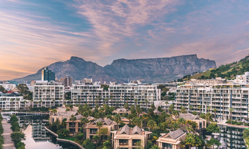 Moderne Wohnanlagen und Villen am Wasser, mit Bergformation im Hintergrund bei Sonnenuntergang.