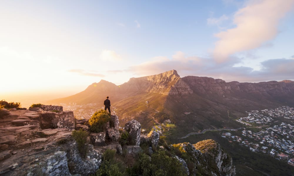 Mann steht auf einem Fels und schaut auf ein Bergpanorama