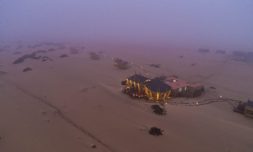 An aerial view of a shipwrecked lodge on the Skeleton Coast with abandoned ships scattered in a desert-like landscape in Namibia.