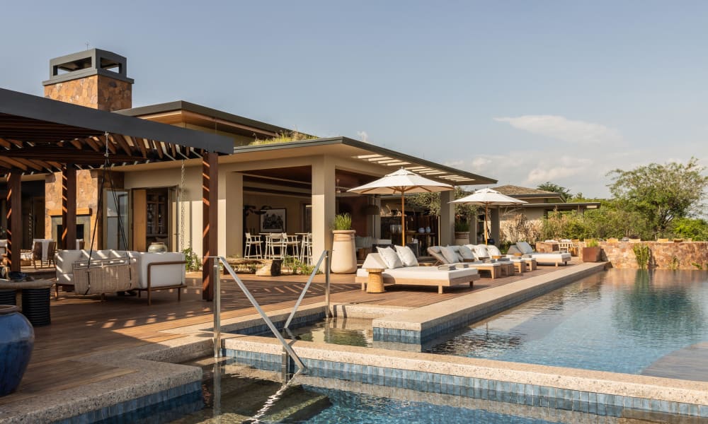 Luxuriöse Poolseite im Freien mit Liegestühlen, Sonnenschirmen und moderner Architektur.