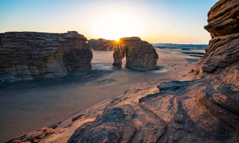Sonnenuntergang, der durch natürliche Steinbögen in einer Wüstenlandschaft in AlUla, Saudi-Arabien, scheint.